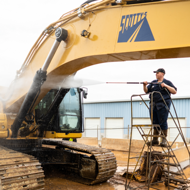 man power washing a construction machine